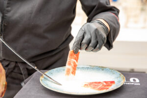 Professional ham slicer placing slices of Iberian ham on a plate